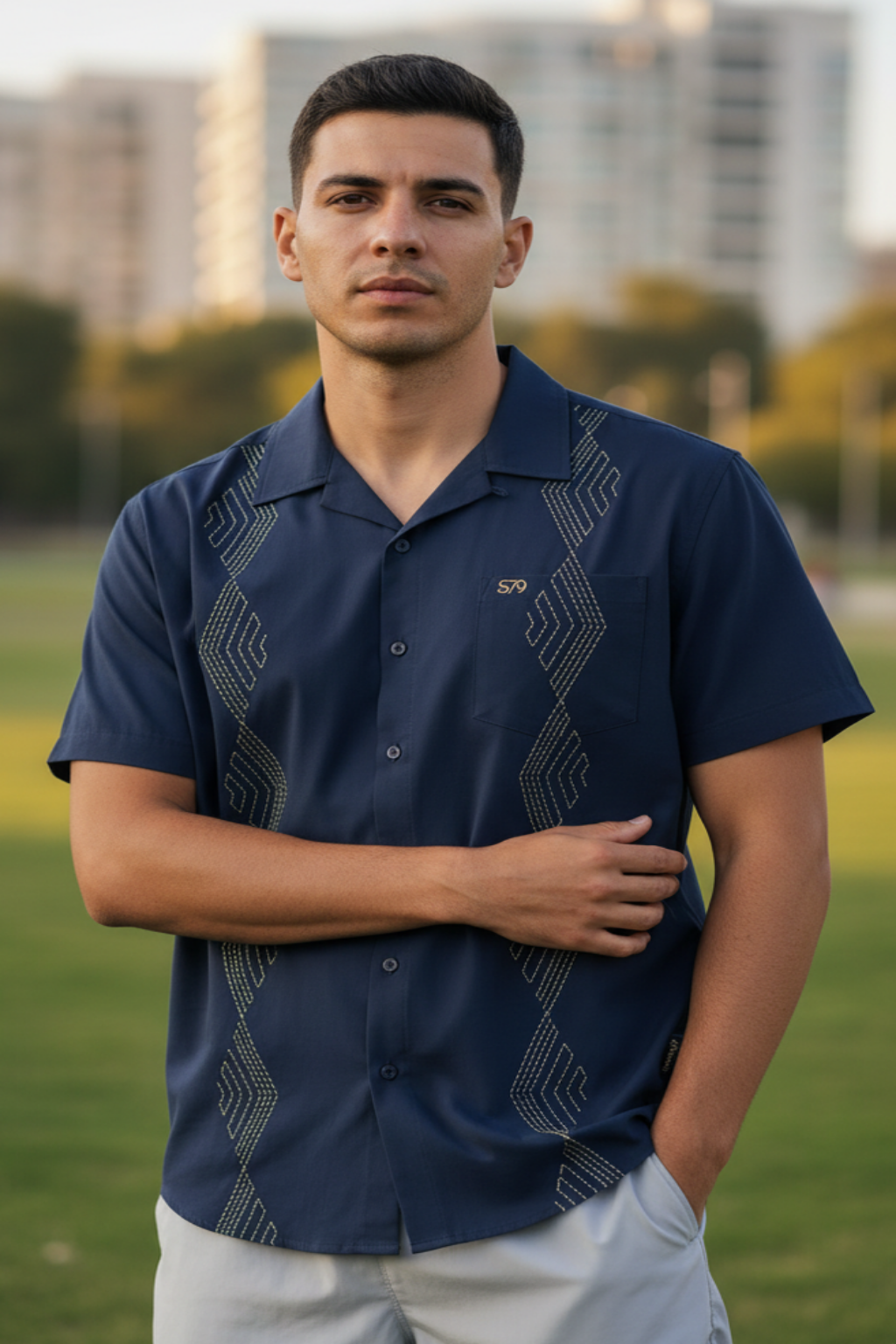 Man wearing a dark blue patterned shirt standing outdoors with blurred buildings in the background