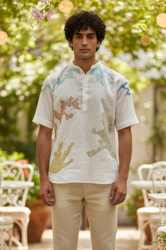 Man wearing a patterned shirt and beige pants standing in an outdoor setting with tables and chairs.